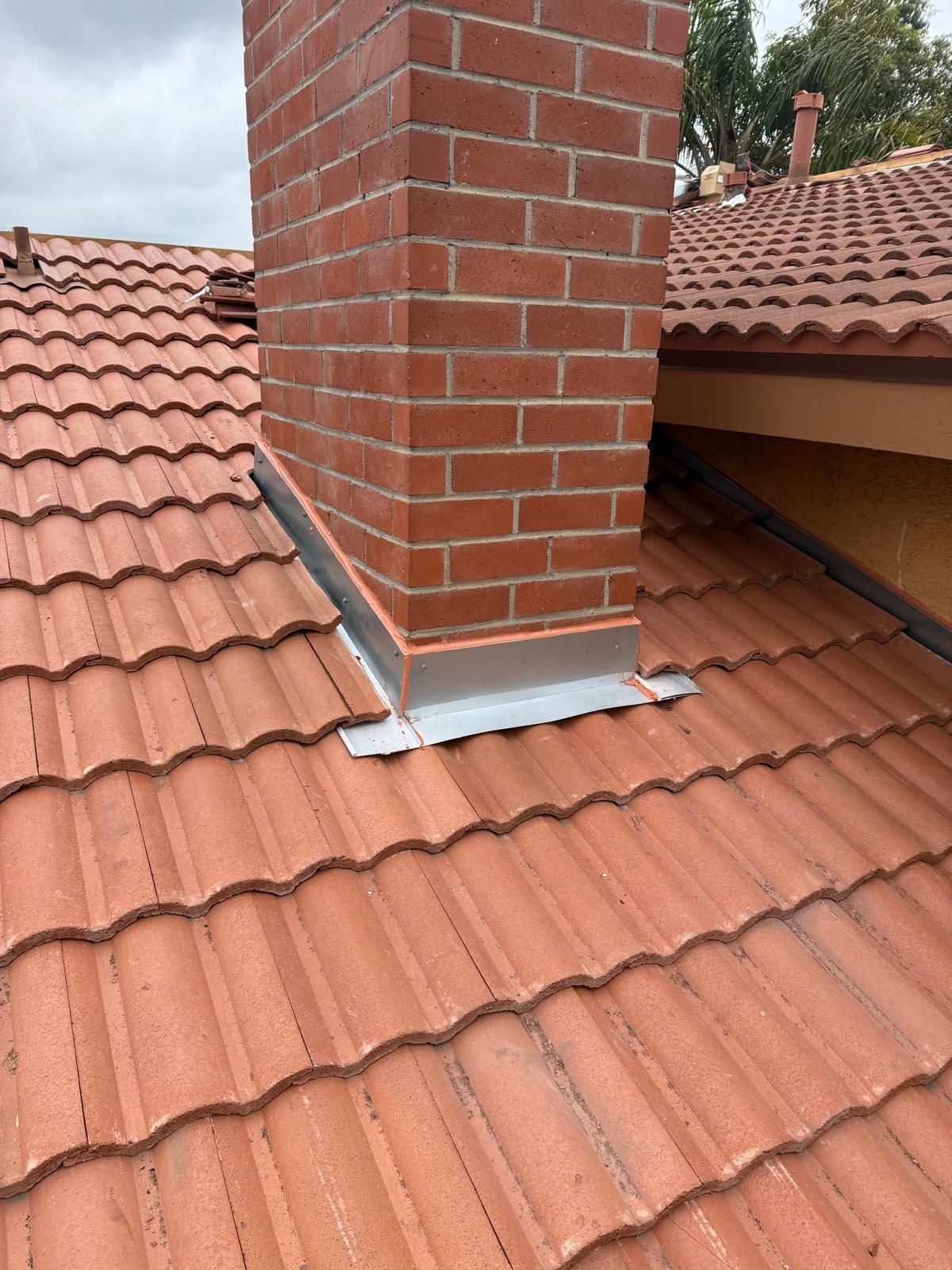 Close view of new sheet metal flashing wrapped and soldered around a brick chimney where it meets fresh roof tile.